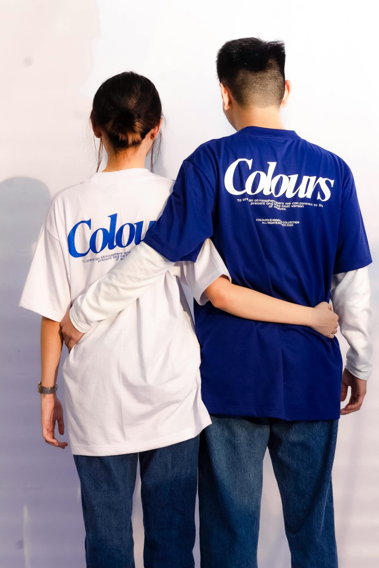 A man and woman with arms around each other, wearing printed T-shirts in a studio.