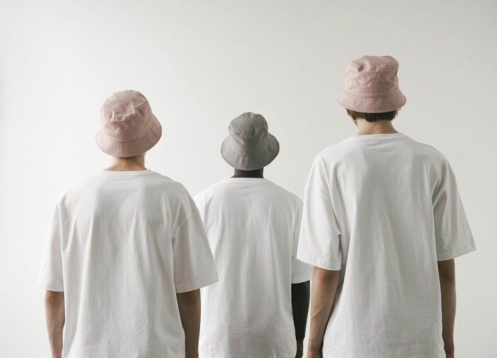 Three men in white shirts and bucket hats facing away against a plain white backdrop.